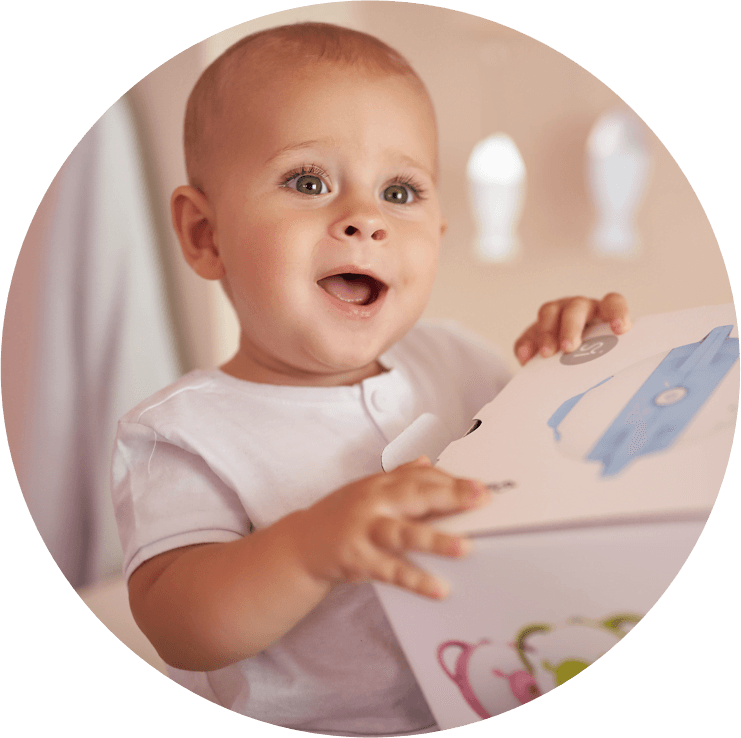 A fascinated baby boy holding a box with the Nosiboo Pro Electric Nasal Aspirator