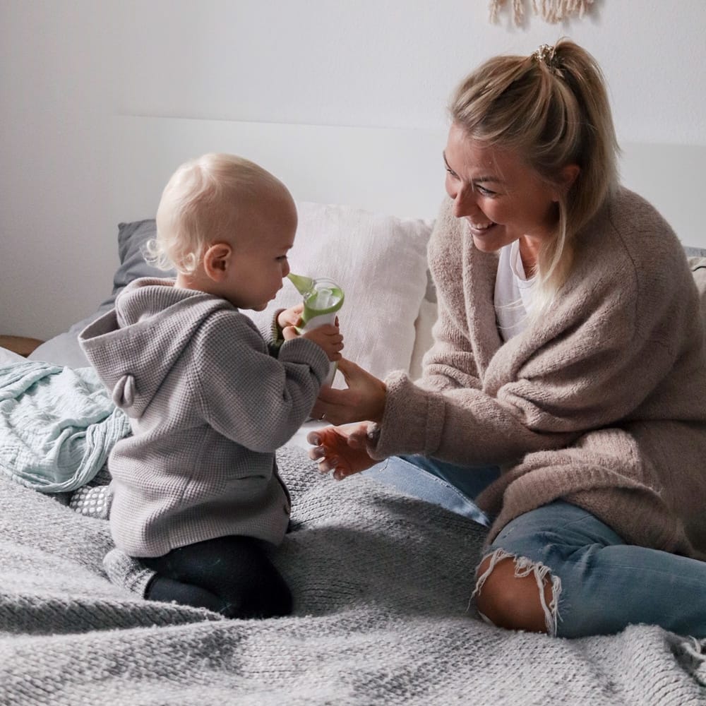 Mom with her son sitting on a bed, aspirating the child's nose with a Nosiboo Pro electric nasal aspirator