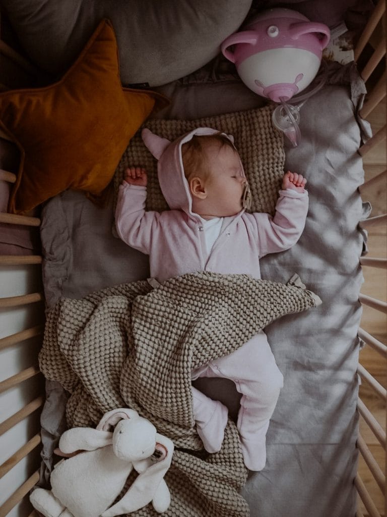 A baby girl sleeping in a Moses basket next to the Nosiboo Pro Electric Nasal Aspirator
