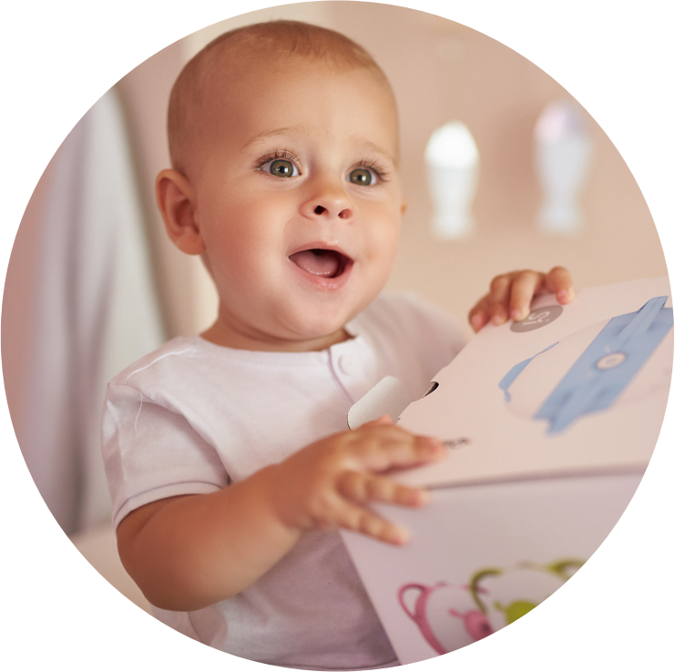 A fascinated baby boy holding a box with the Nosiboo Pro Electric Nasal Aspirator