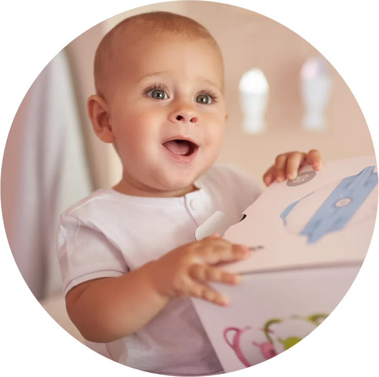 A fascinated baby boy holding a box with the Nosiboo Pro Electric Nasal Aspirator