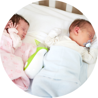 Zwei Neugeborene in Rosa und Blau schlafen im Babybett mit dem tragbaren Baby Nasensauger Nosiboo Go zwischen ihnen