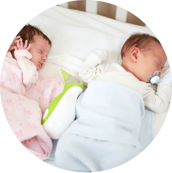 Two newborns lying in the baby cot bed with the Nosiboo Go Portable Nasal Aspirator