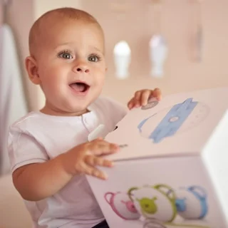 A fascinated baby boy holding a box with the Nosiboo Pro Electric Nasal Aspirator