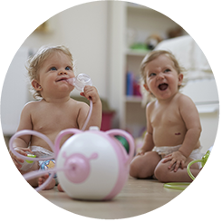 Two happy baby girls sitting on the floor with the Nosiboo Pro Electric Nasal Aspirator