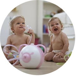 Two happy baby girls sitting on the floor with the Nosiboo Pro Electric Nasal Aspirator