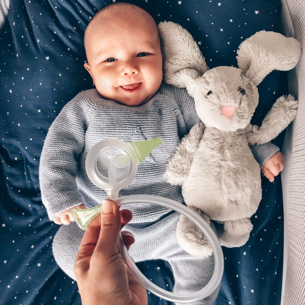 Somebody holding a Nosiboo Eco manual nasal aspirator above a smiling baby