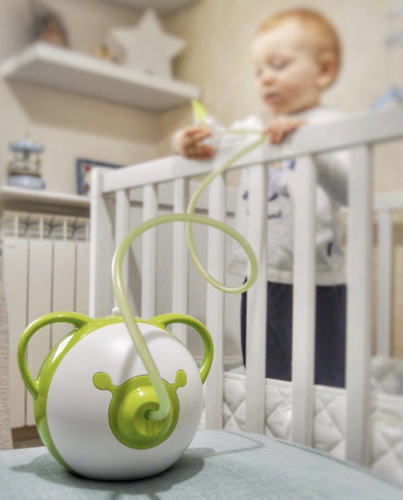 Green Nosiboo Pro electric nasal aspirator, with a little boy standing on a bed in the background
