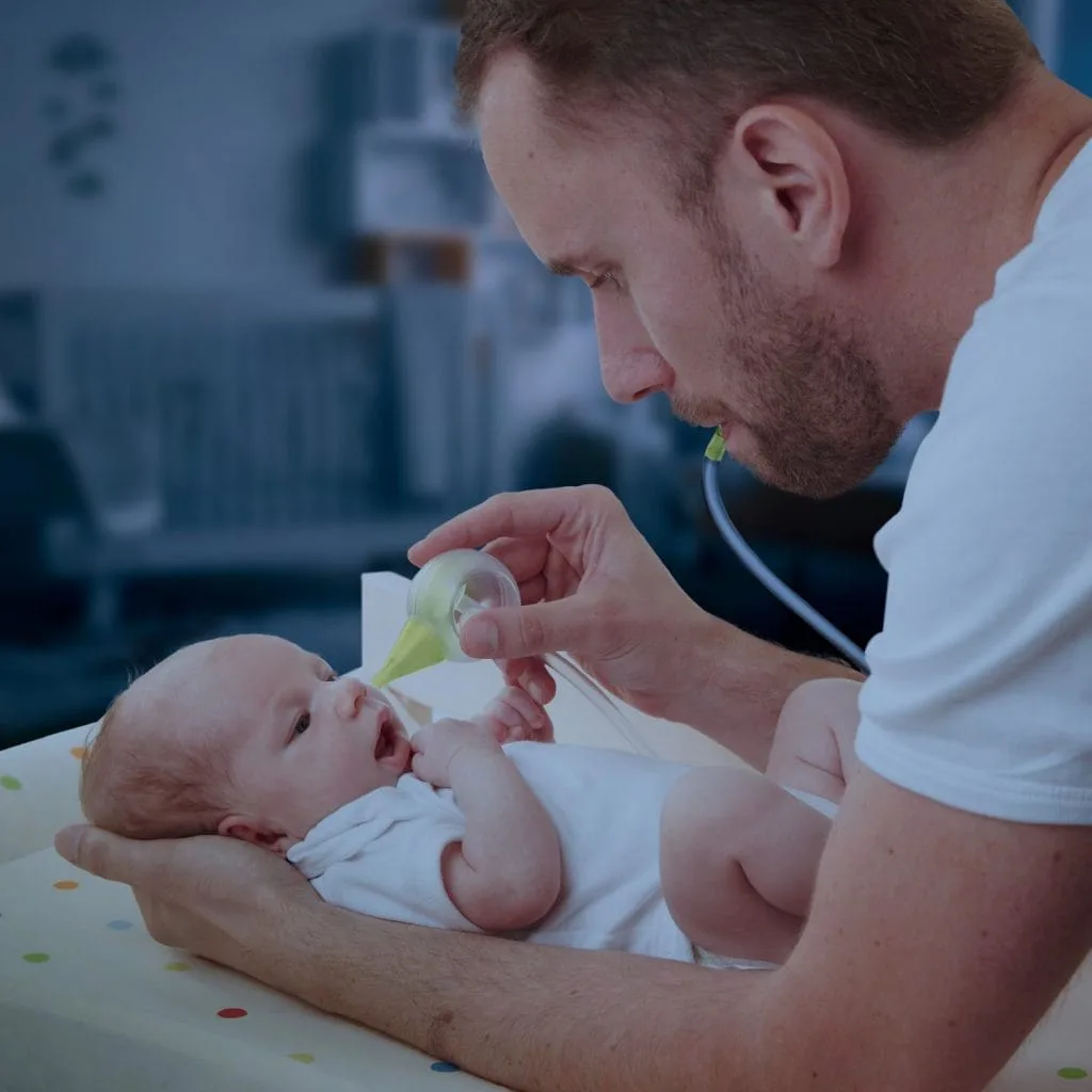 Dad holding a newborn and aspirating his nose with a Nosiboo Eco manual nasal aspirator