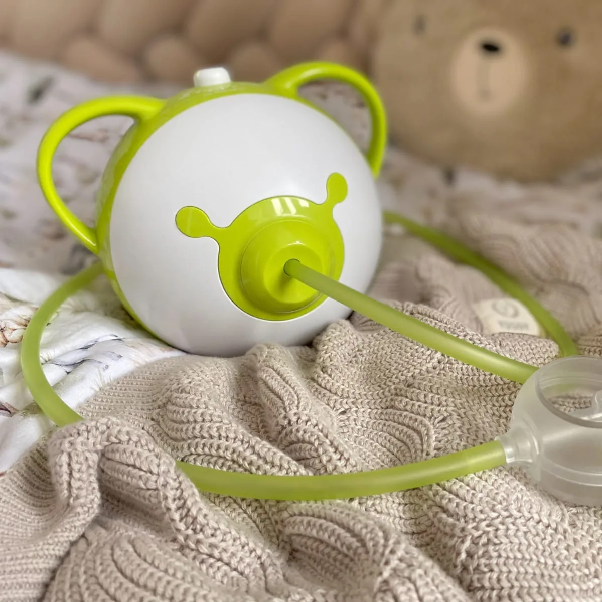 A green Nosiboo Pro2 electric nasal aspirator on a bed.